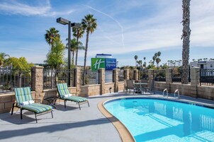 Un área de piscina con sillones de descanso, un letrero de Holiday Inn Express y palmeras.
