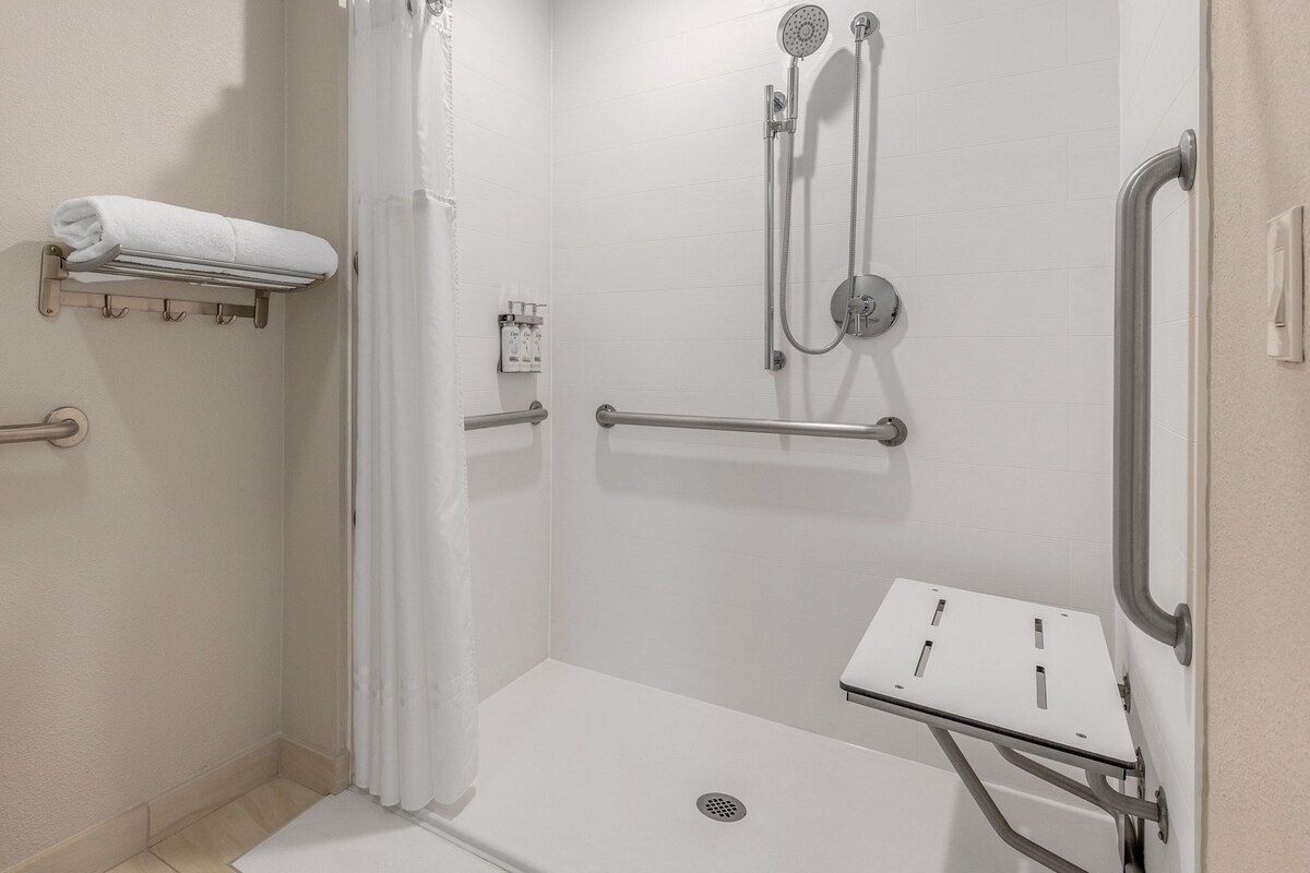 Une salle de bain moderne dotée d’une douche à l’italienne, de barres d’appui, d’un porte-serviettes et d’un pommeau de douche amovible.