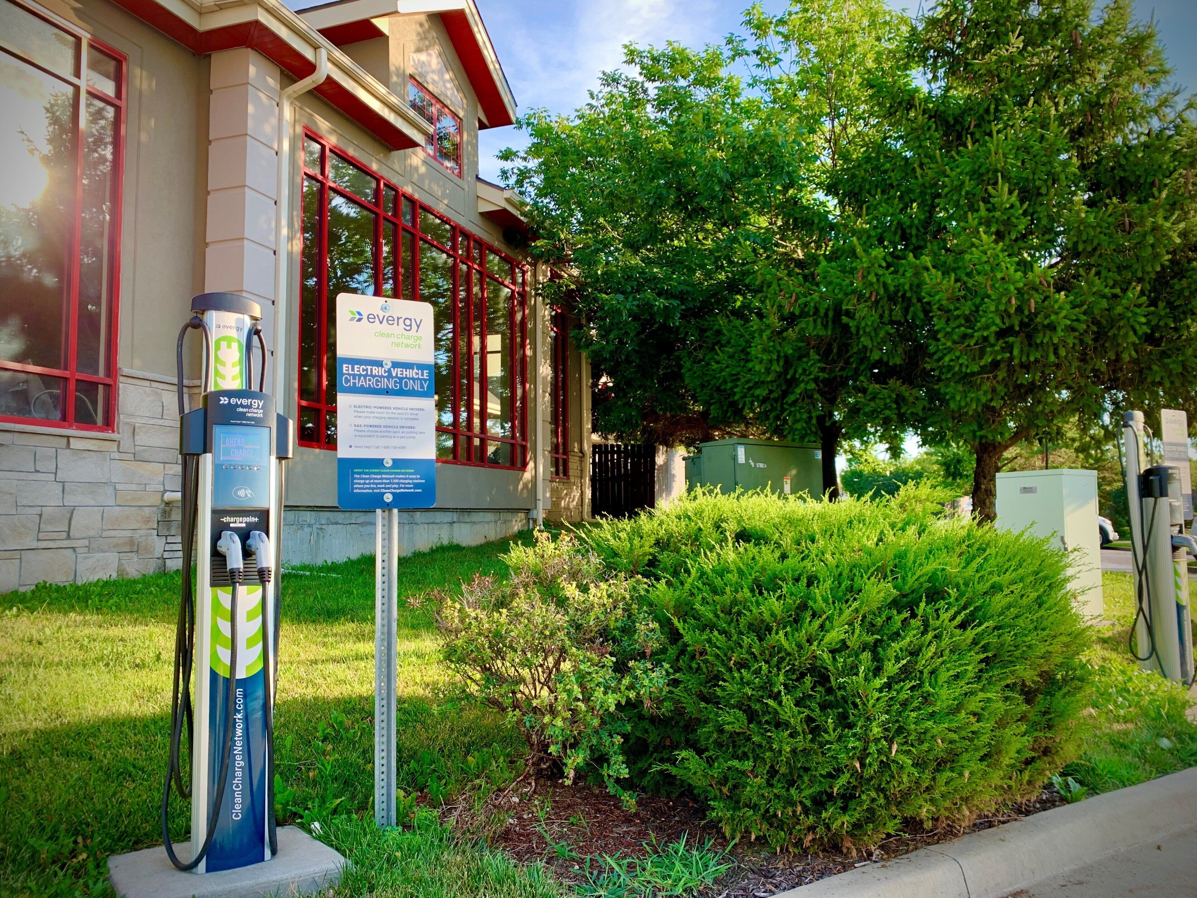 A clean electric vehicle charging station in front of a building with red-framed windows and a green lawn.