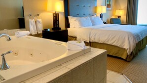 A hotel room with a large bathtub, two bedside lamps, a bed with white linens, and a headboard. - Holiday Inn Express Hotel & Suites Olathe North by IHG (Olathe)