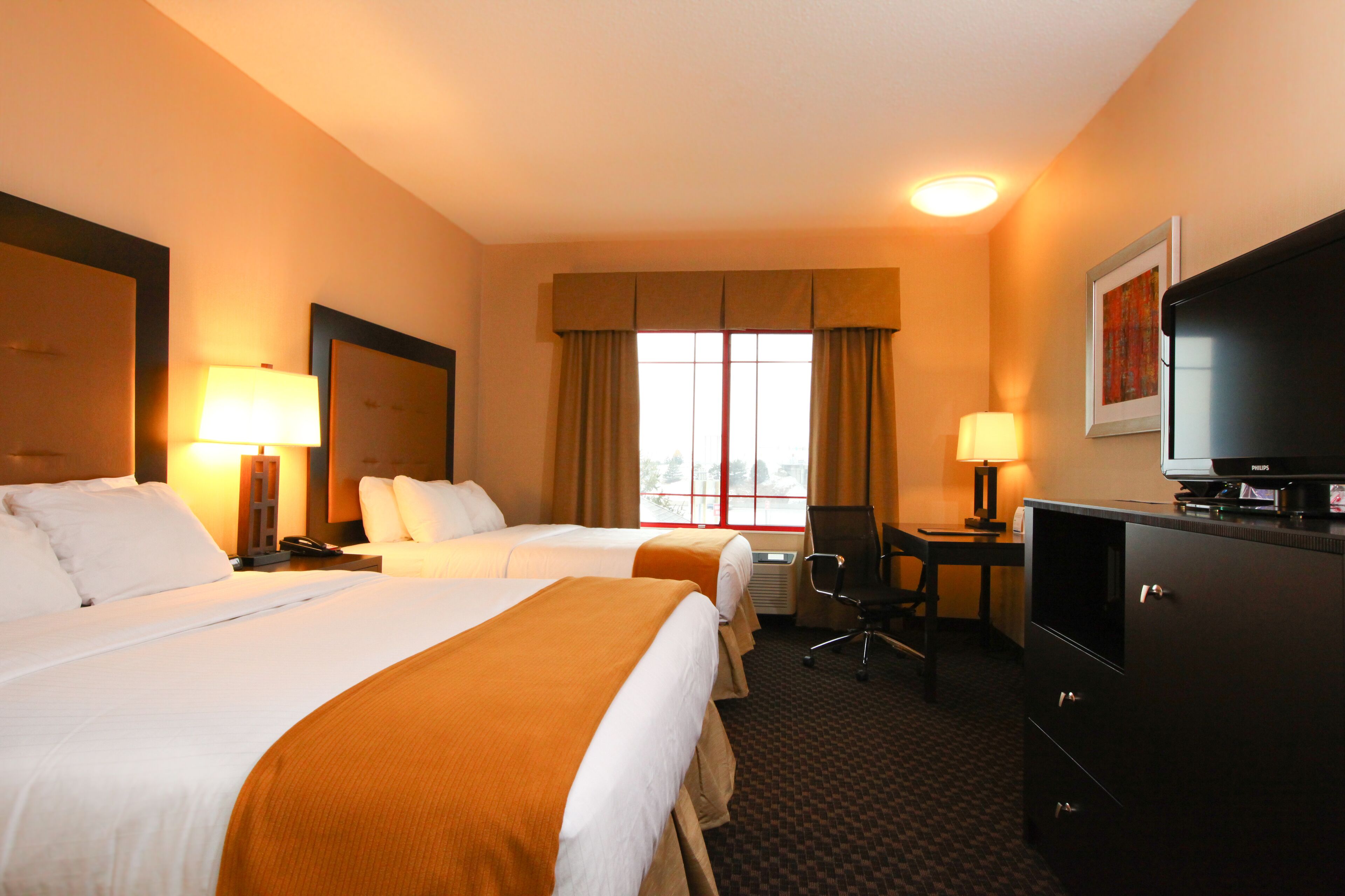 A hotel room with two beds, a desk, a chair, a television, and a window with curtains.