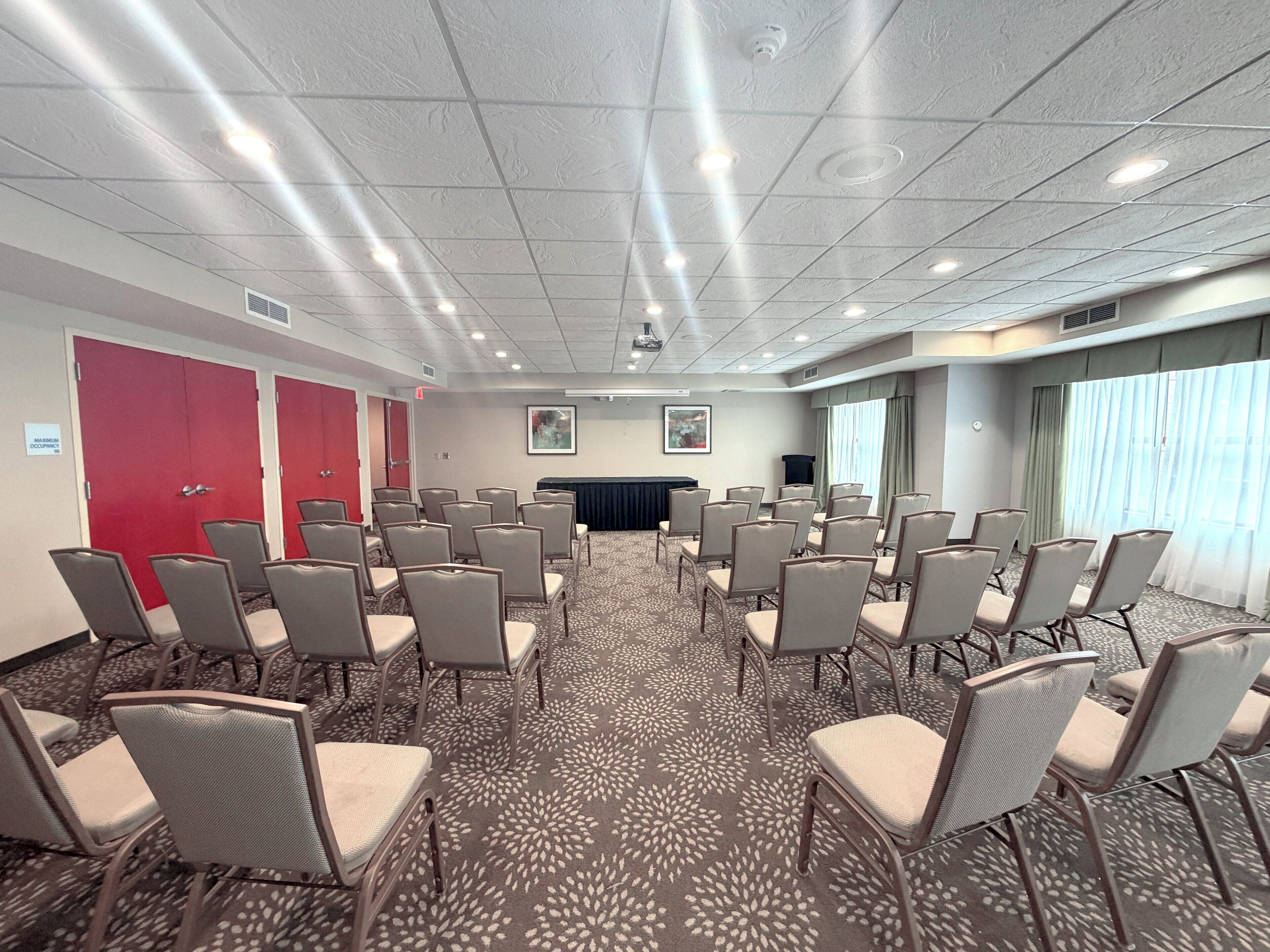 Een congreszaal met rijen stoelen, een spreekgestoelte en een groot raam met gordijnen.