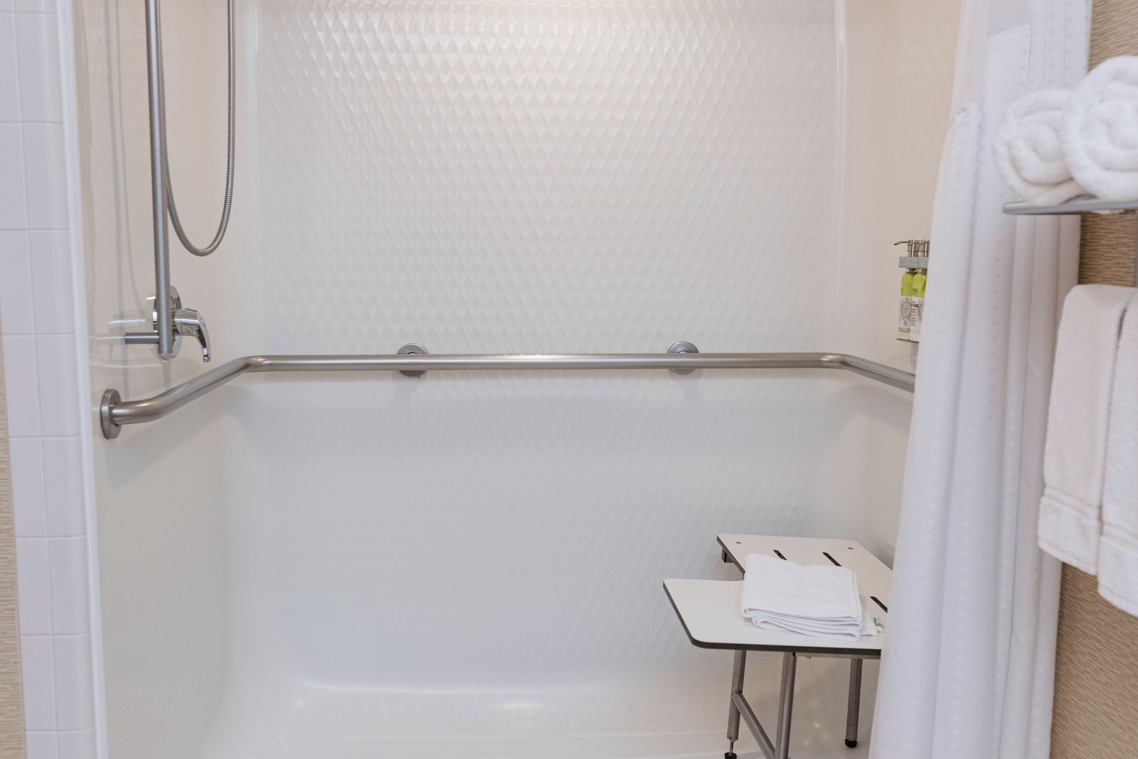 A shower area with a glass door, a handrail, and a small table with towels.