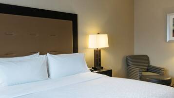 Quarto de hotel com uma cama grande, mesa de cabeceira com abajur e uma cadeira.