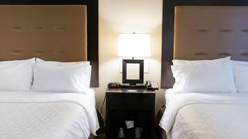 Una habitación de hotel con dos camas, una mesita de noche con lámpara, teléfono y un pequeño cofre.
