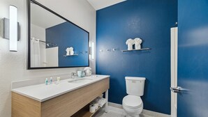 A modern bathroom with a double sink vanity, a large mirror, a toilet, and a blue accent wall. - Spark by Hilton Houston near the Galleria (Houston)