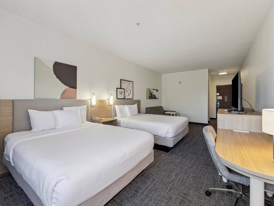 Habitación de hotel con dos camas, un escritorio, una silla y un televisor.