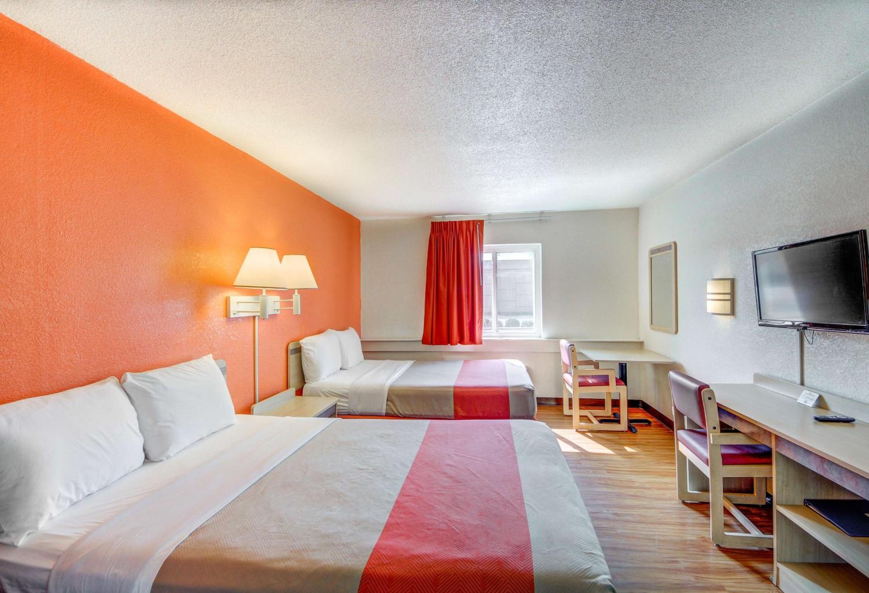 A hotel room with two beds, a desk, a chair, a TV, and a window with curtains.