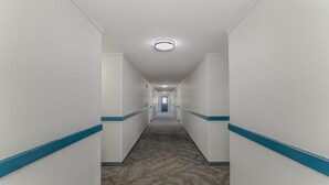 A long, narrow hallway with white walls and blue trim, leading to a door at the end. - Motel 6 Wichita, KS (Wichita)