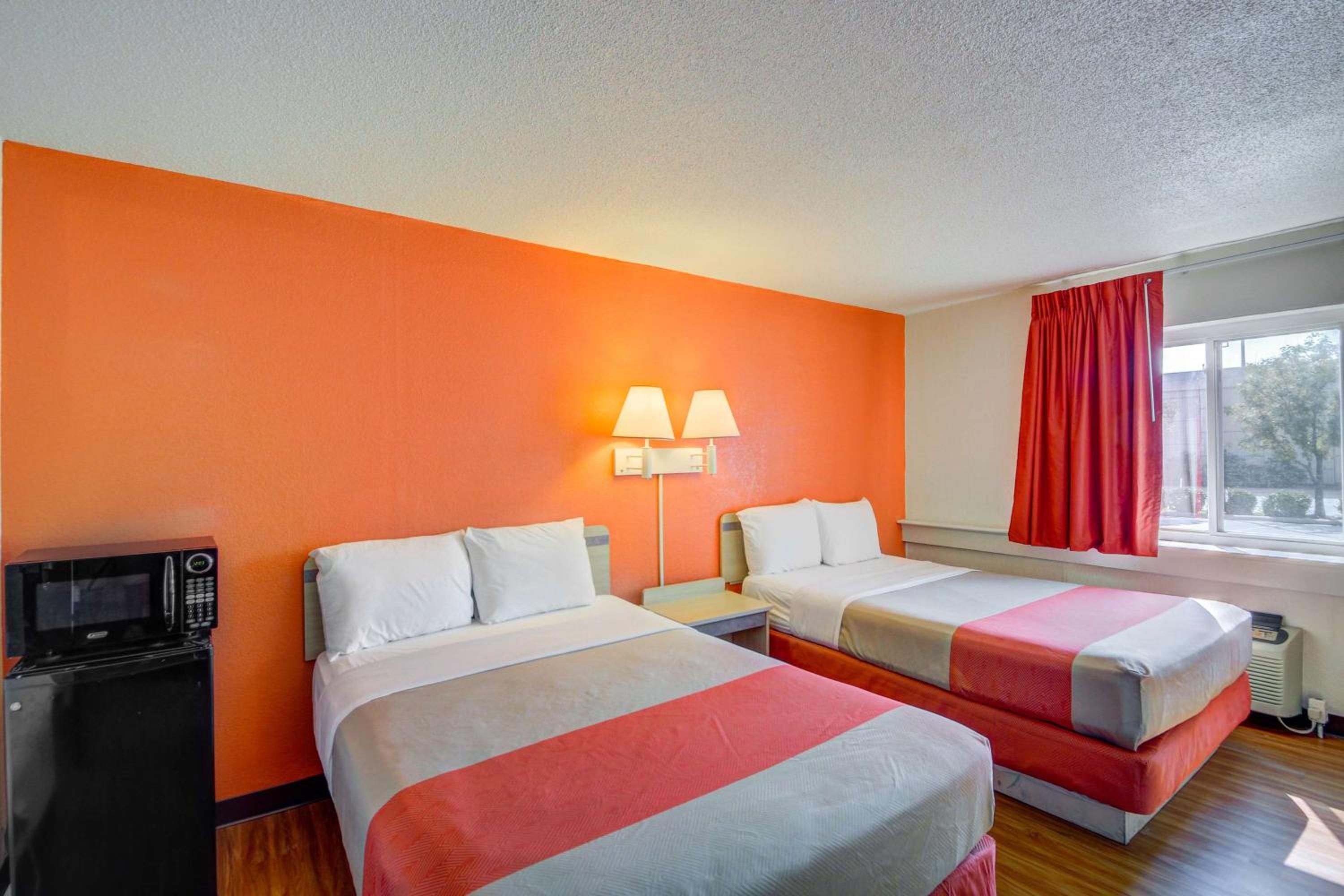 A hotel room with two beds, a microwave, a nightstand, and a window with curtains.