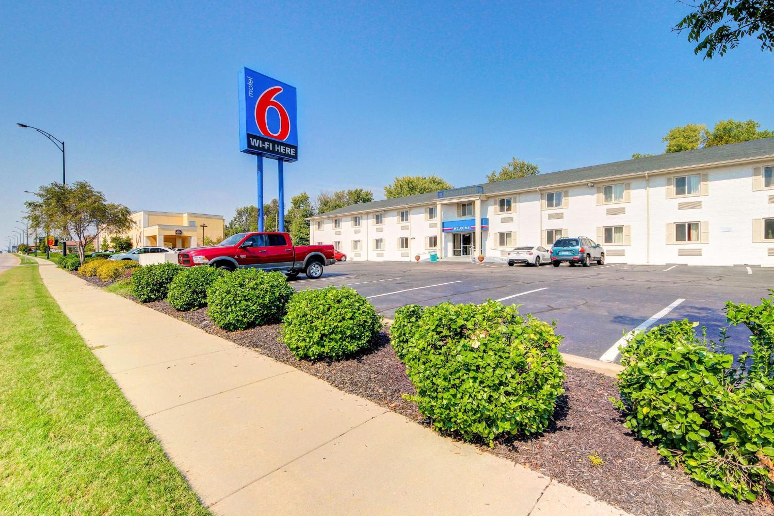 A motel with a blue sign, a parking lot, and a building with a 'Welcome' sign.
