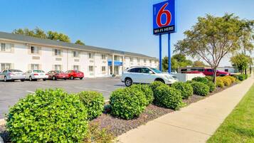 A motel with a large blue sign indicating it is number 6. There are several cars parked in front, and the building has a simple, functional design with a flat roof.