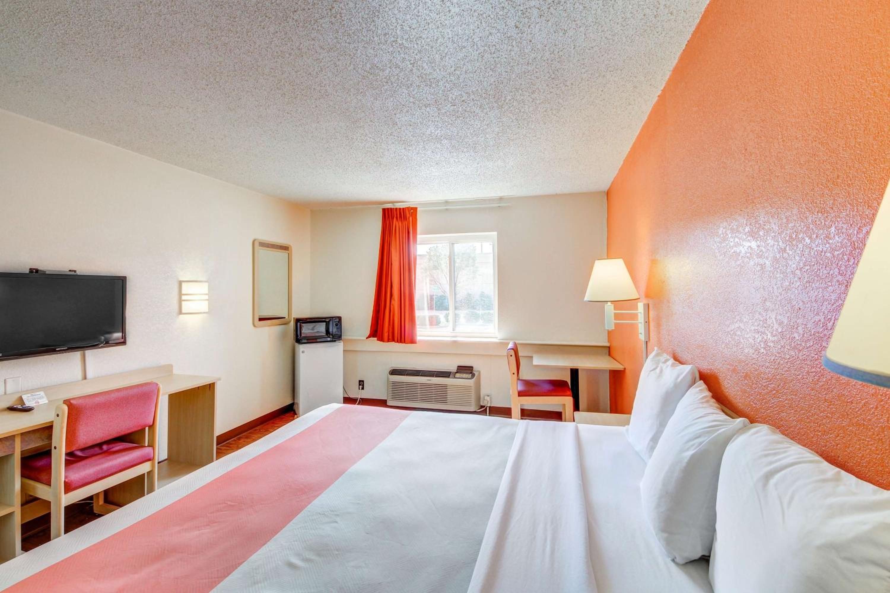 A hotel room with a bed, desk, chair, television, and a window with curtains.
