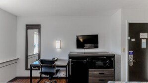 A hotel room with a desk, chair, TV, microwave, and a door with a security lock. - Motel 6 Wichita, KS (Wichita)