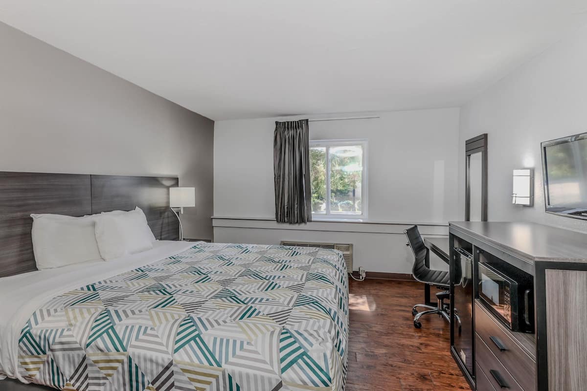 A hotel room with a bed, a desk, a chair, a window with curtains, and a television.