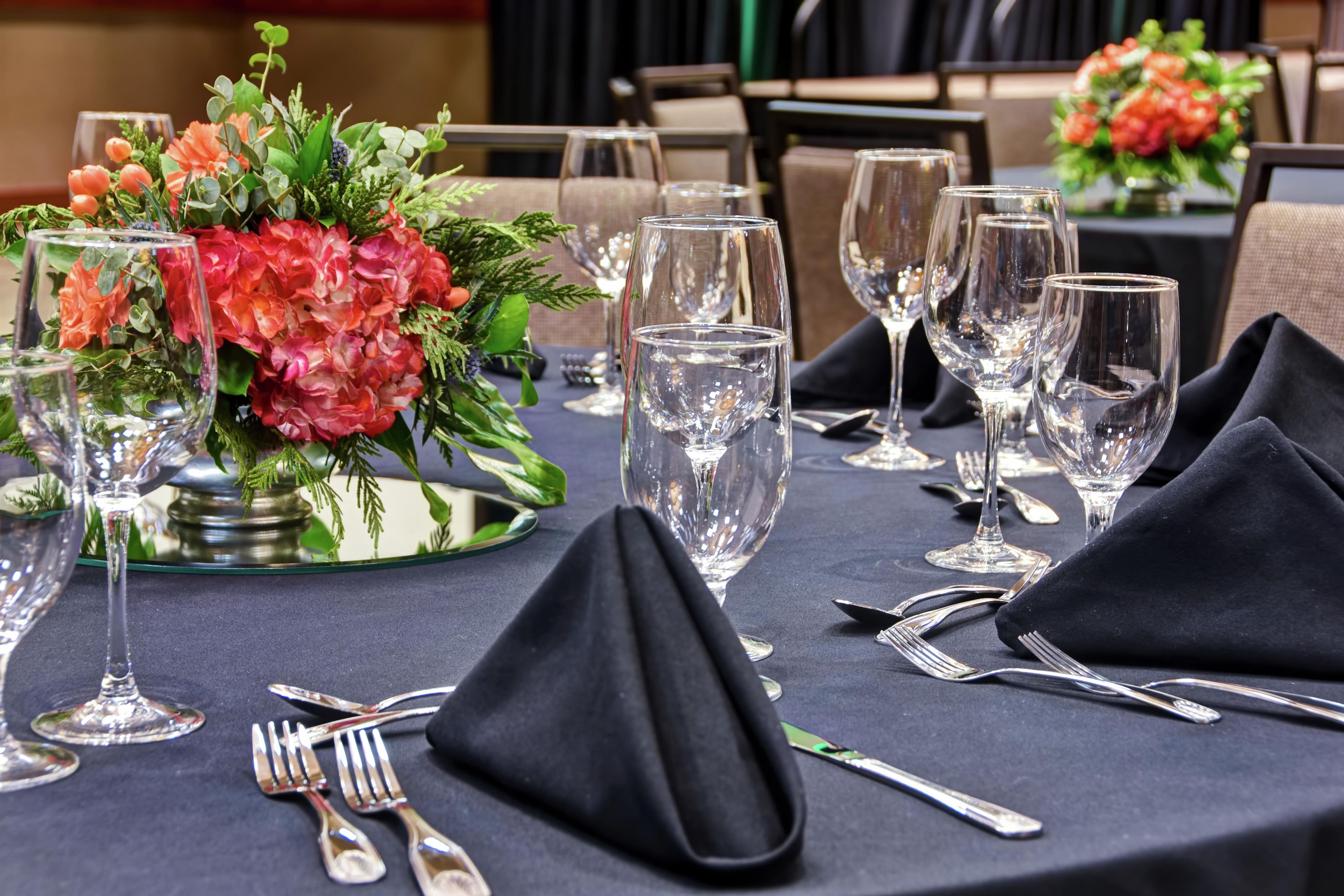 Une table dressée pour le repas, agrémentée d’un centre de table composé de fleurs, de verres transparents et de couverts disposés avec soin.