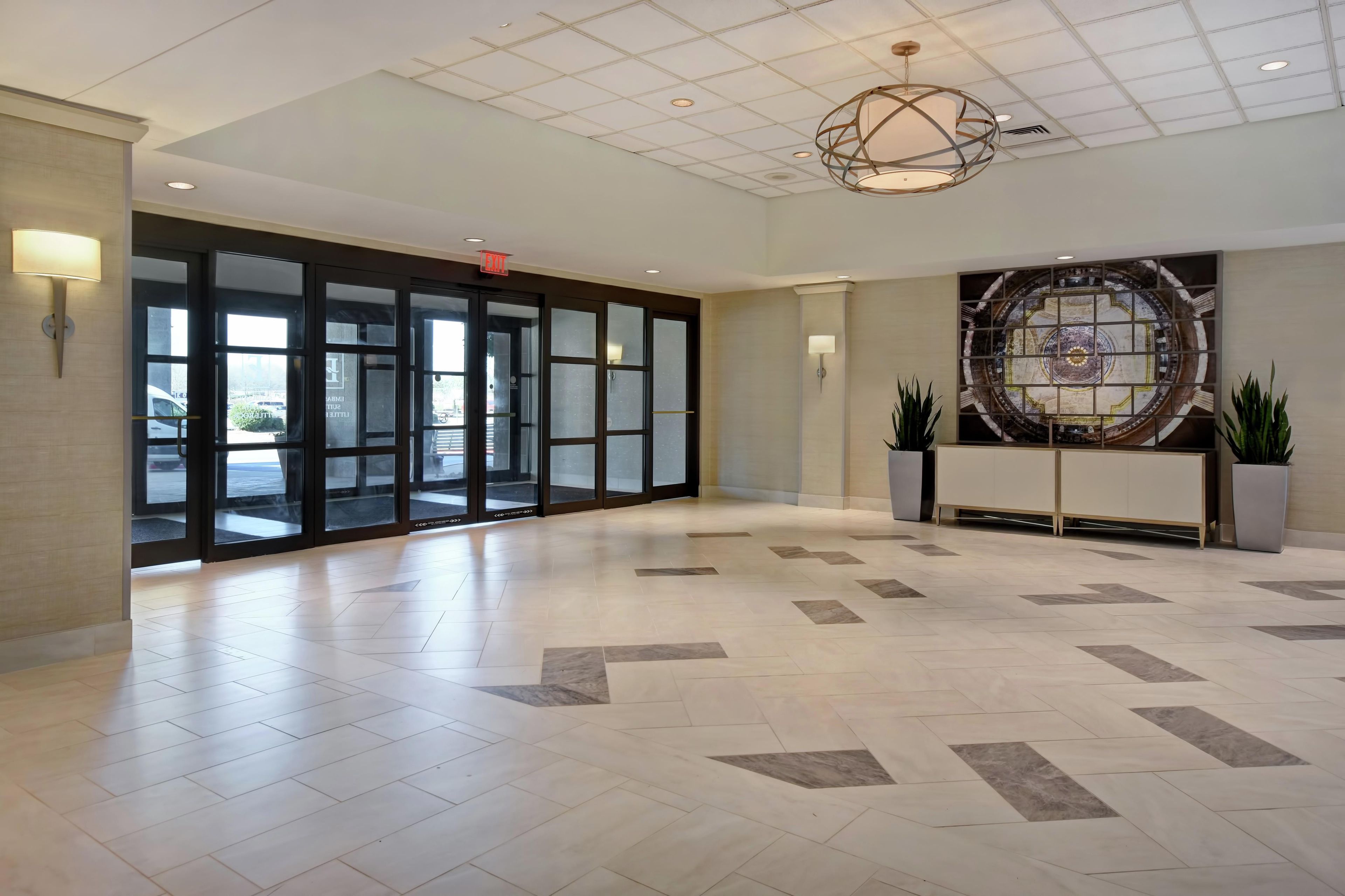 Um hall amplo com piso ladrilhado, porta de entrada de vidro e luminária decorativa no teto.