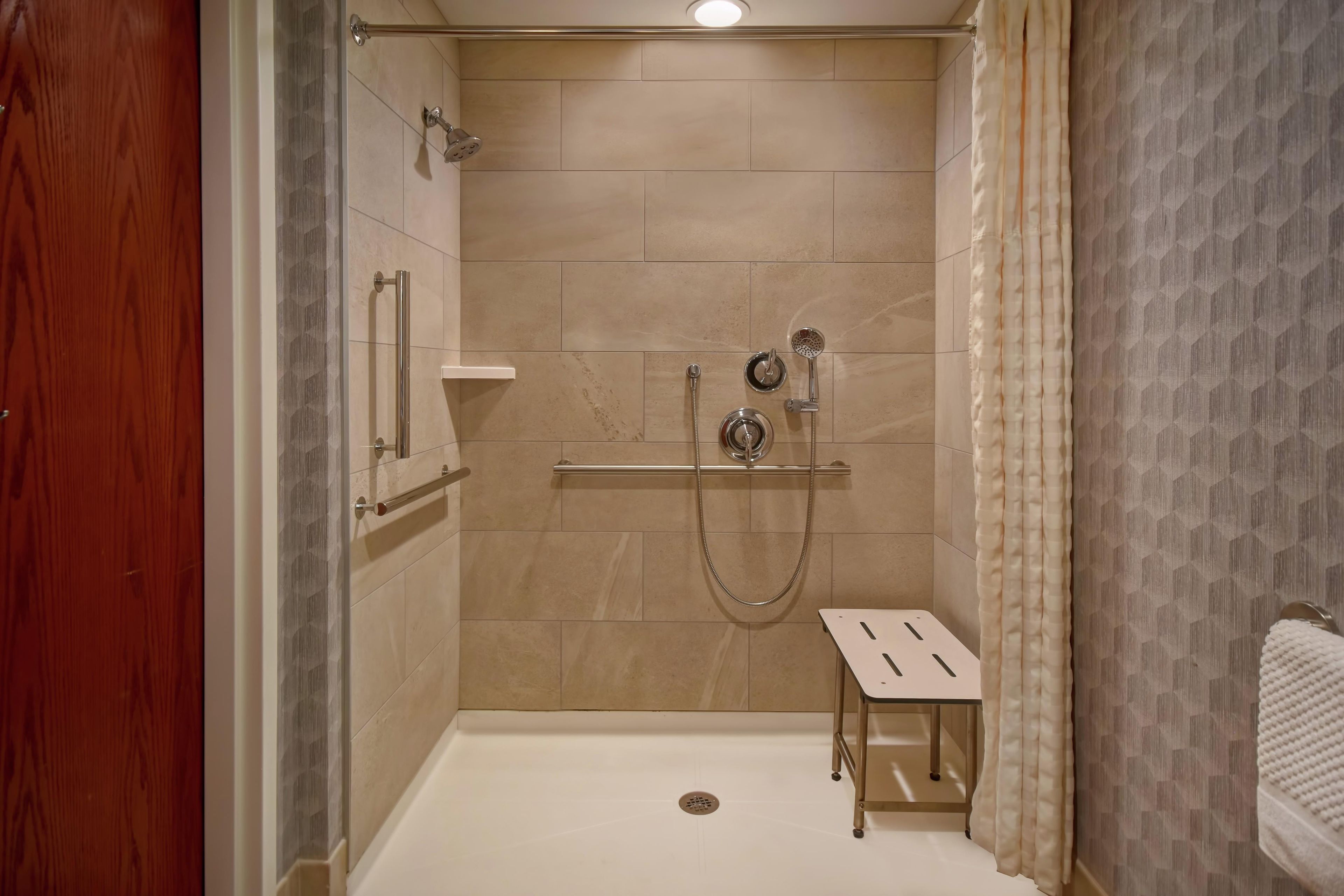 Une douche à l’italienne avec une porte en verre, un pommeau de douche amovible, un robinet mural et un petit marchepied.