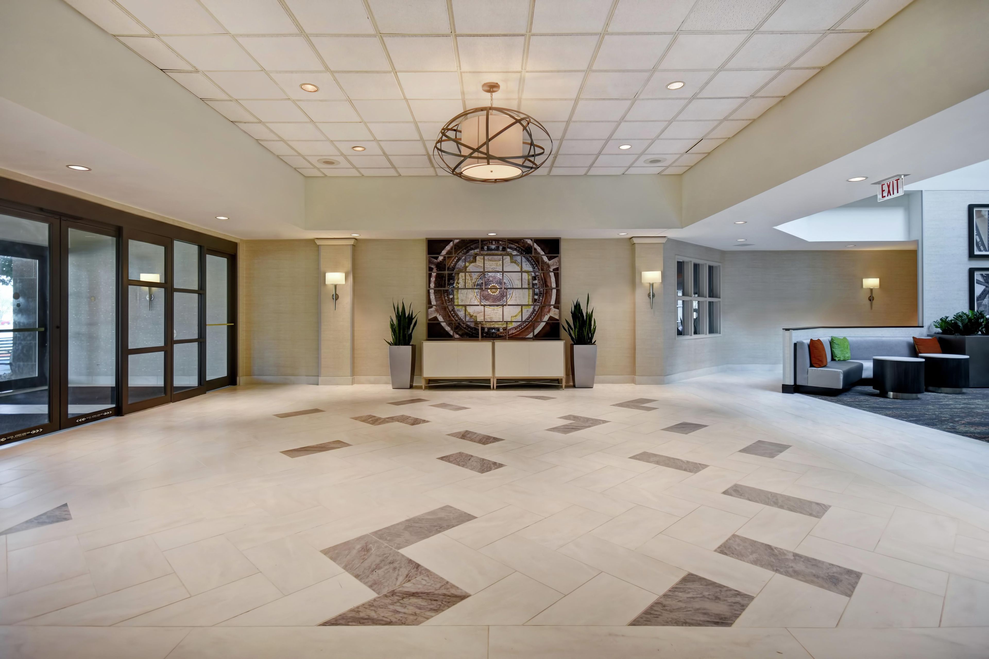 A spacious lobby with a modern chandelier, a reception desk, and a large wall mural.
