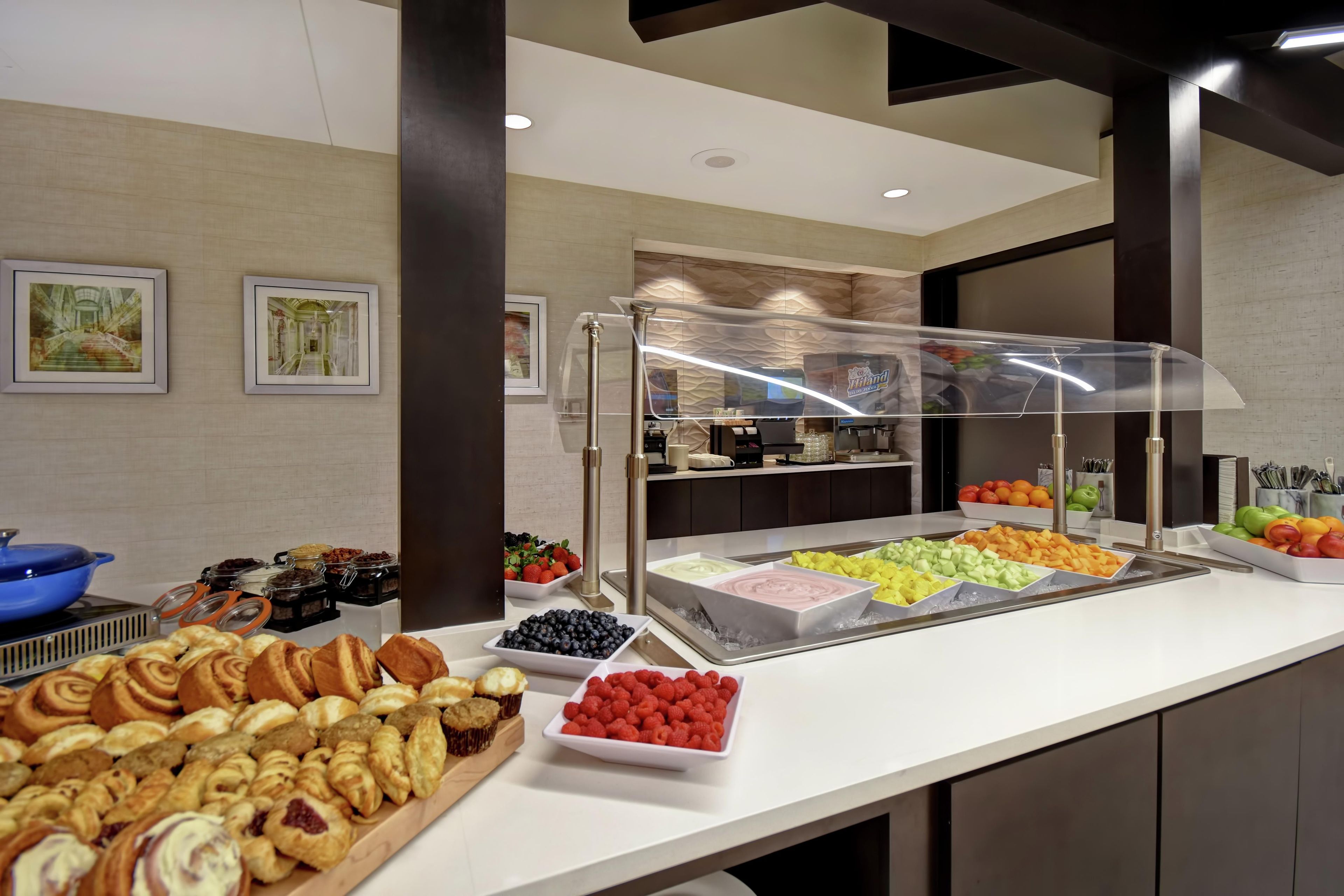 Un bufé con diversas opciones de comida, incluyendo pastelería, frutas y una estación de café.