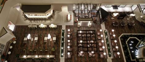 A spacious hotel lobby with multiple seating areas, a central staircase, and a decorative ceiling.