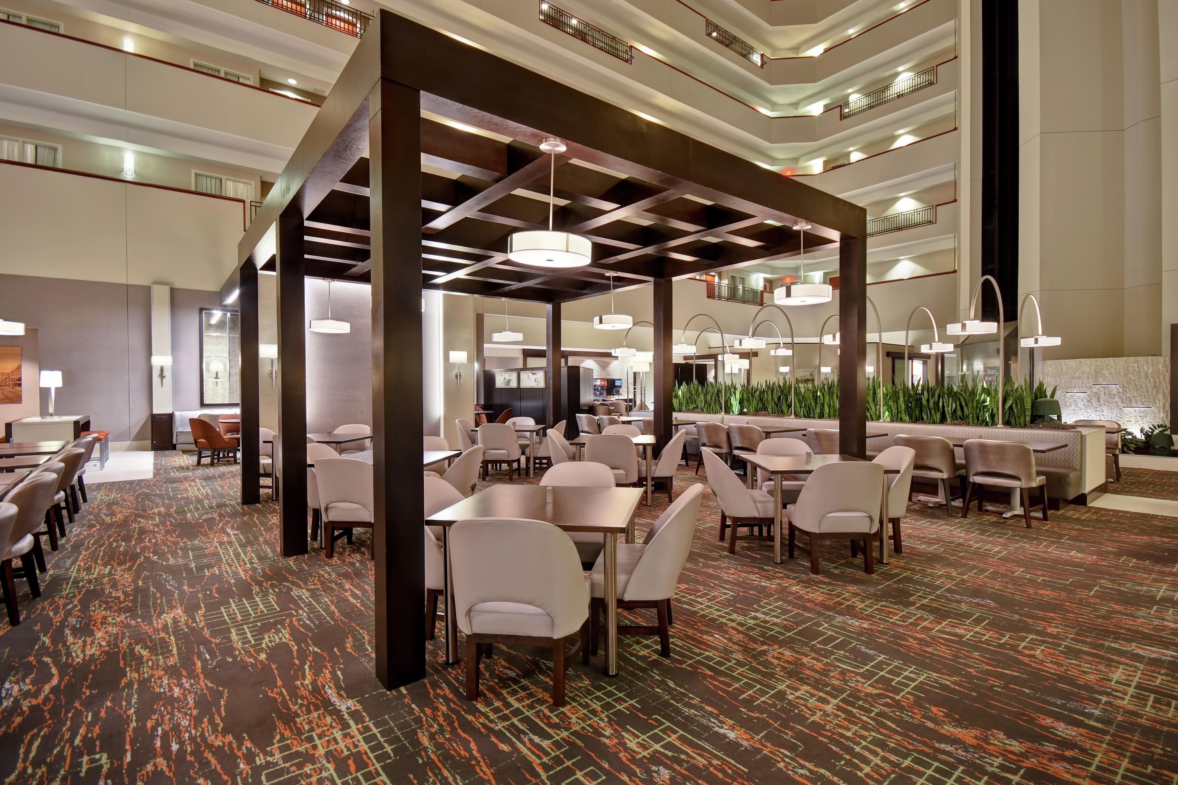A spacious hotel lobby with multiple seating areas, a central bar, and a high ceiling with modern lighting fixtures.