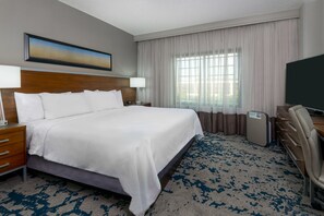 A hotel room with a large bed, a desk, a chair, a television, and a window with curtains. - Embassy Suites Little Rock (Little Rock)