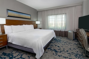 Habitación de hotel con una cama grande, un escritorio, una silla, un televisor y una ventana con cortinas.