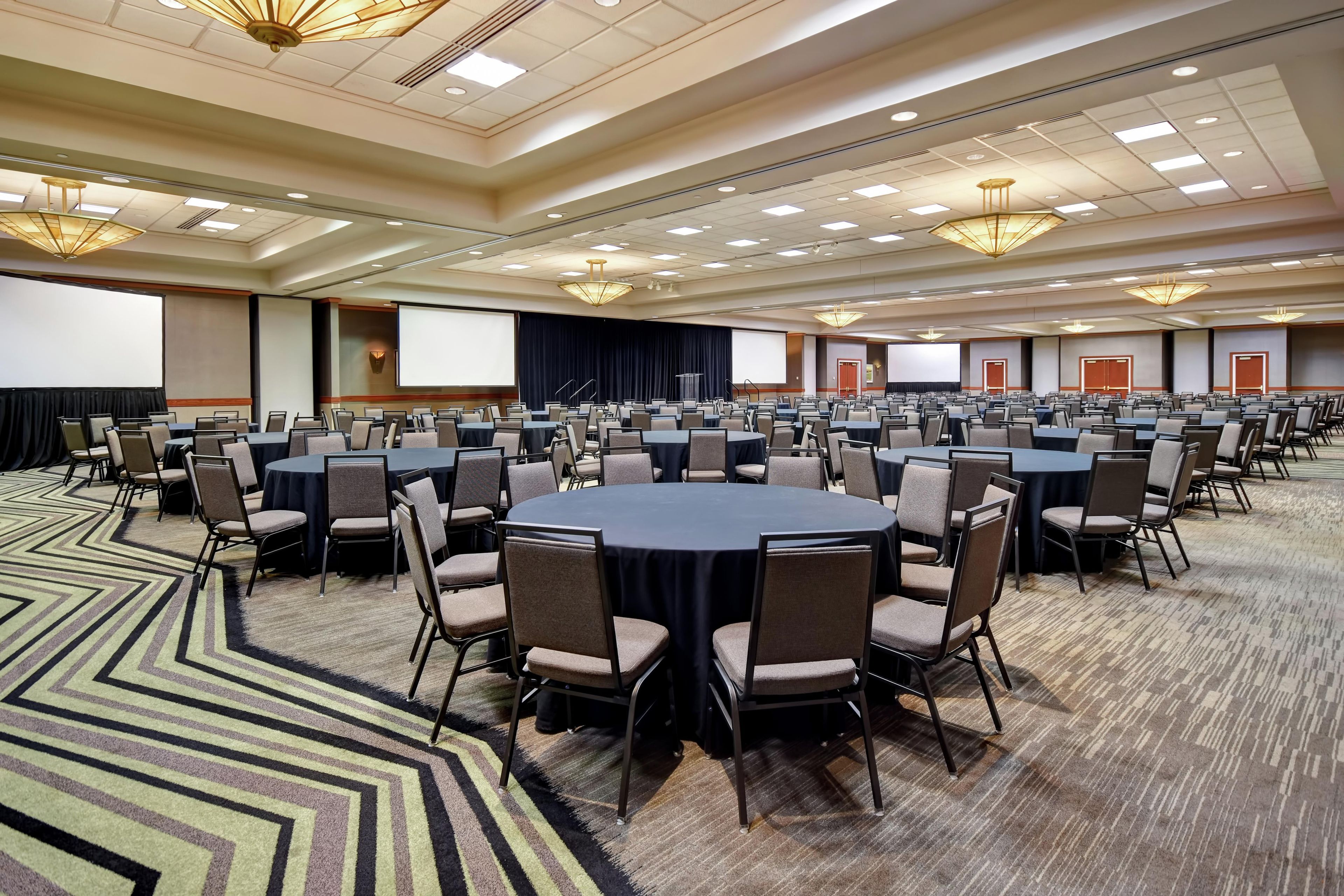 A large conference room with multiple tables and chairs, equipped with projectors and screens.