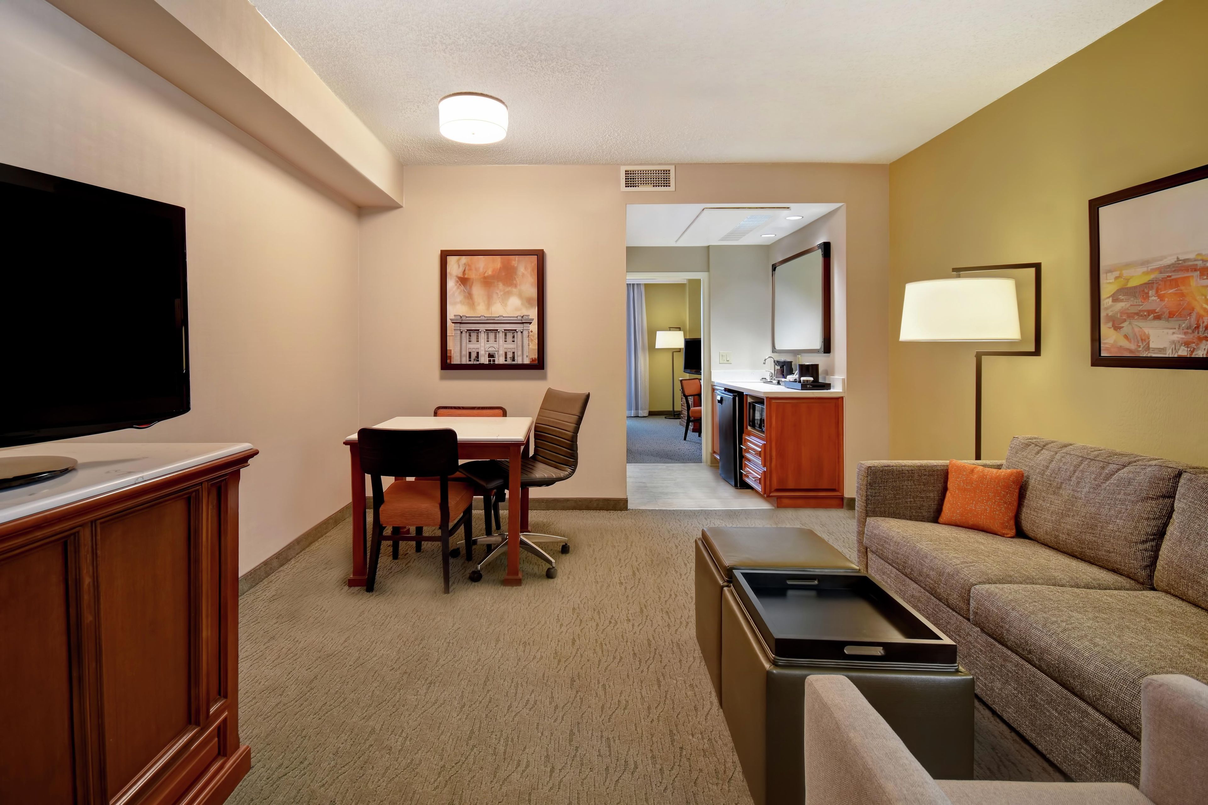 A hotel room with a television, a dining table with chairs, a sofa, a coffee table, and artwork on the walls.