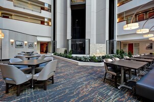 Un vestíbulo de hotel con varias zonas de estar, una pared decorativa central y una alfombra estampada.