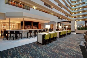 A hotel lobby with a bar area, seating, and a high ceiling with multiple levels.