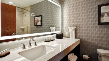 A modern bathroom with a large mirror, a sink with two faucets, a toilet, and a shower area.