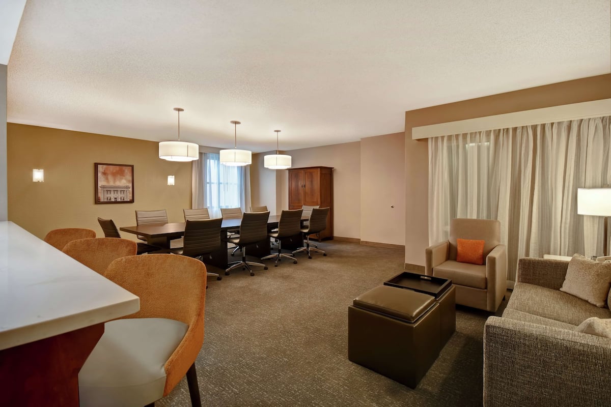 A hotel room with a dining area, a sofa, a chair, and a desk.