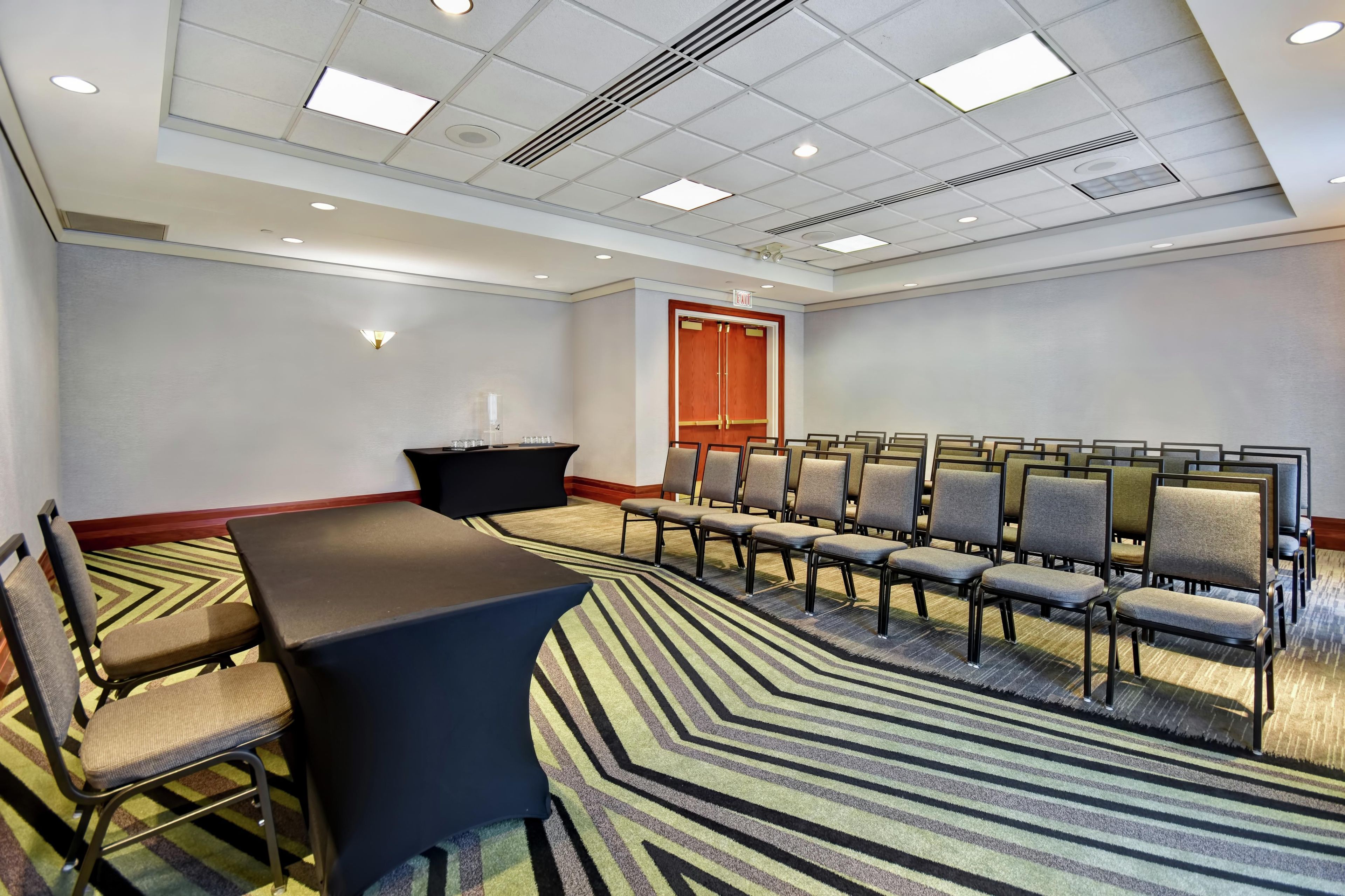 A conference room with a long table, rows of chairs, a carpeted floor, and a ceiling with recessed lighting.