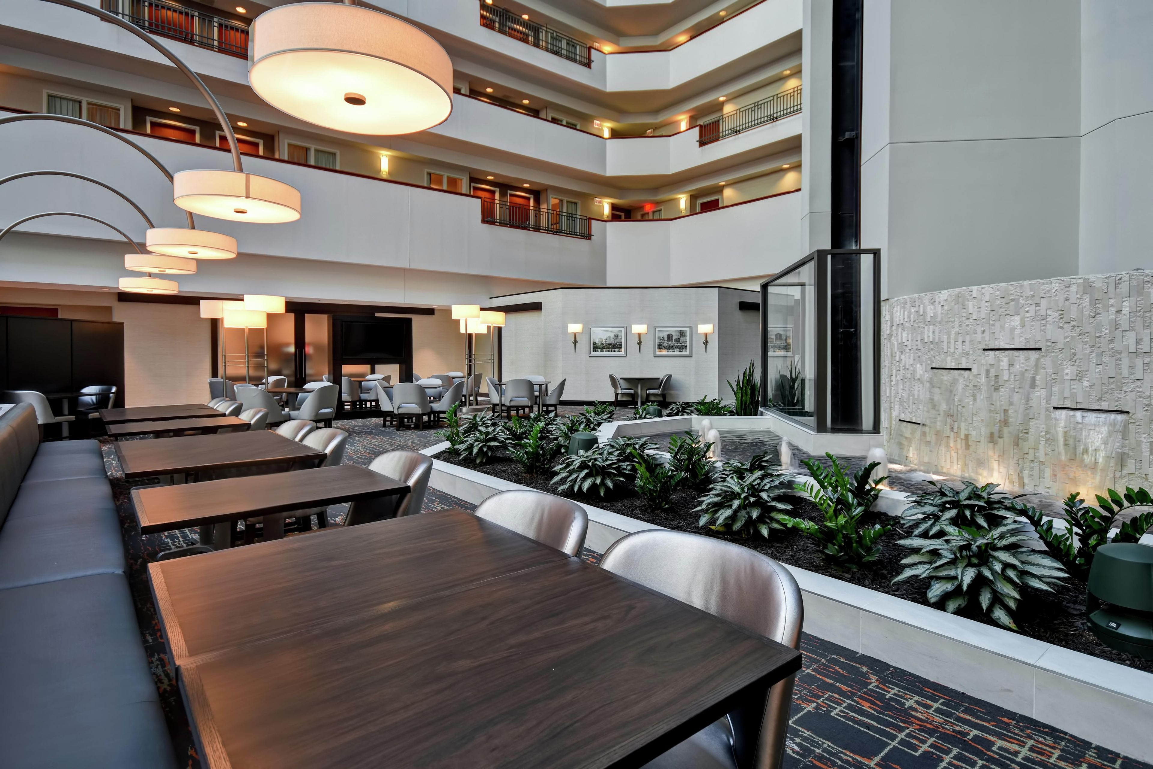 A multi-level hotel lobby with dining areas, a water feature, and a modern design.
