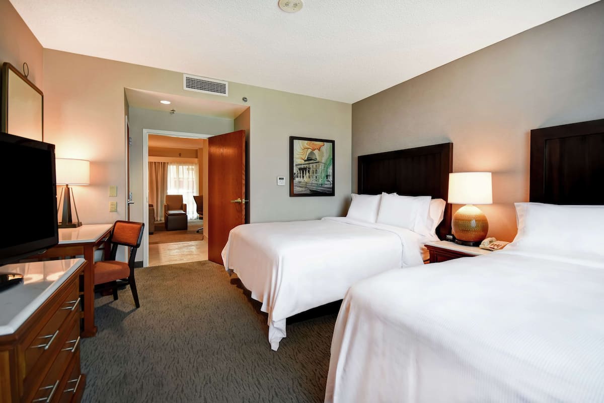 A hotel room with two beds, a desk with a chair, a television, and a painting on the wall.