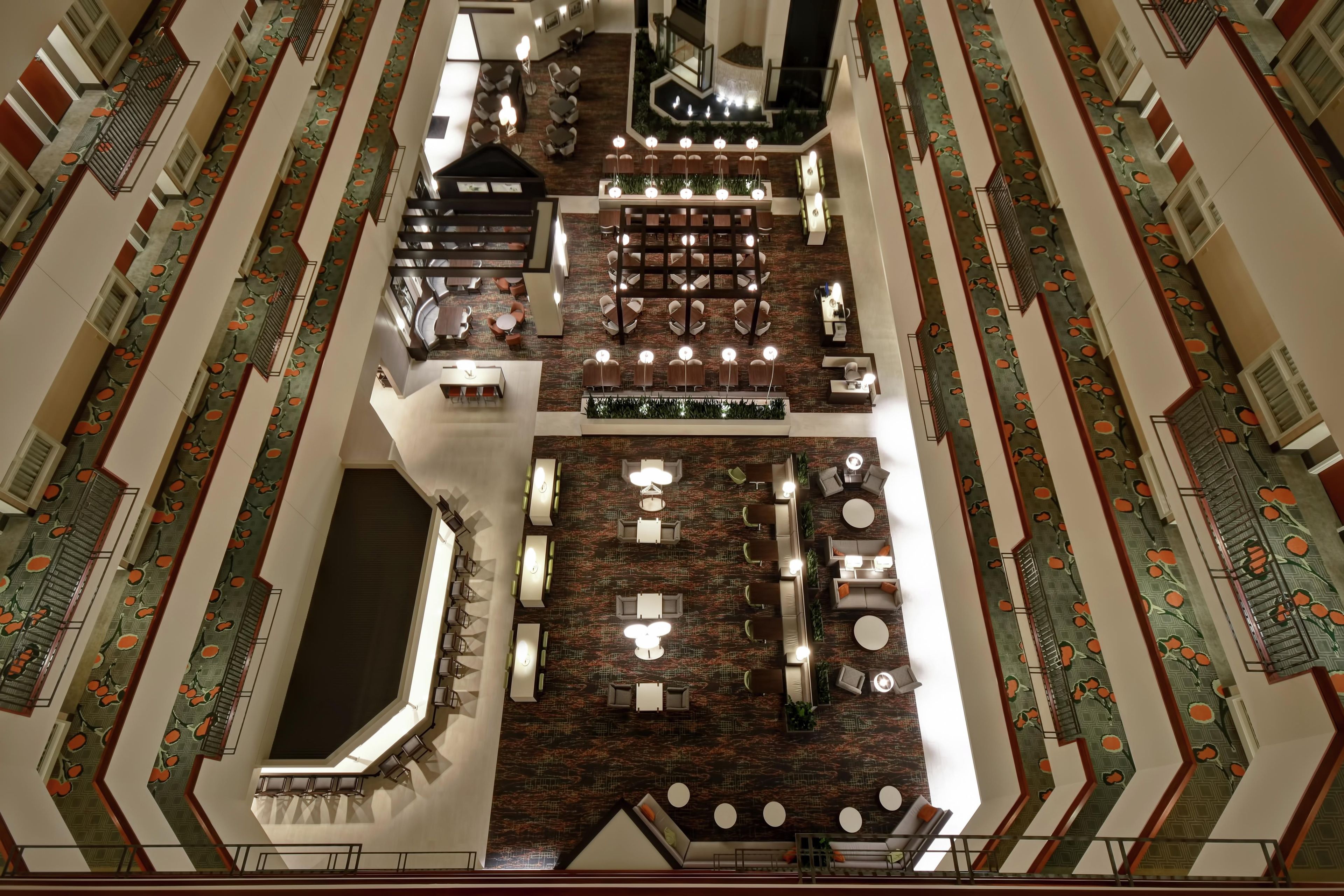 Un hall d’hôtel doté d’un espace salon central, de plusieurs tables à manger et d’un escalier.