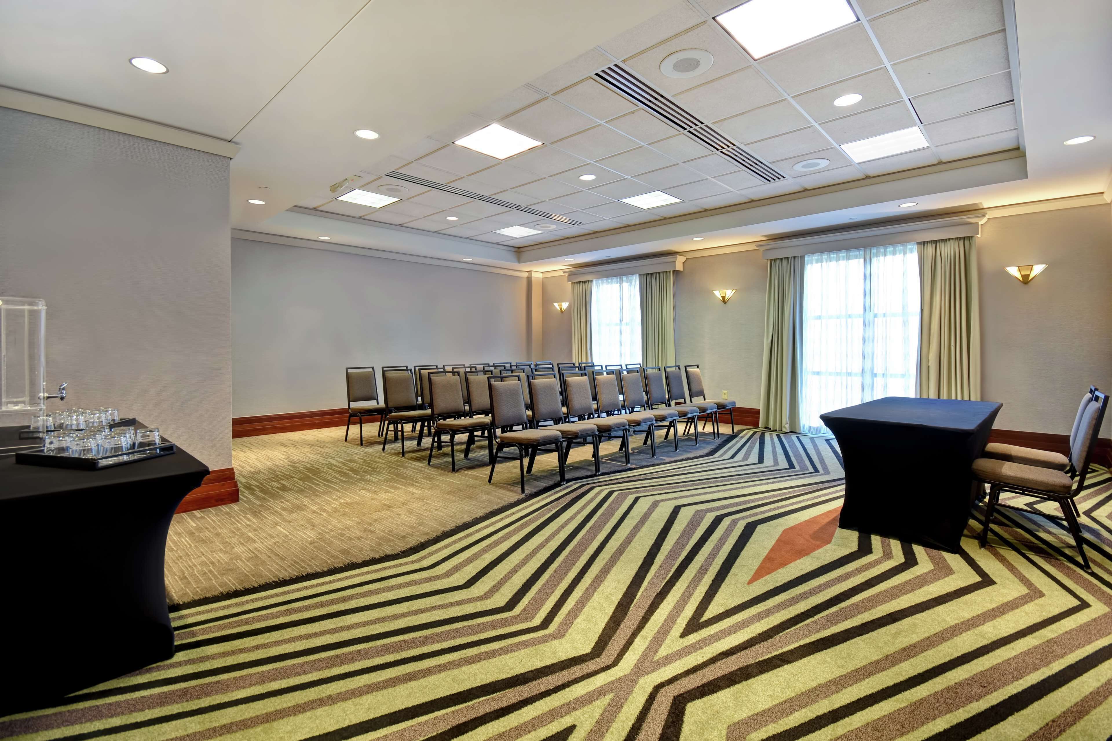 A conference room with a carpeted floor, rows of chairs, a table with a black tablecloth, and a window with curtains.