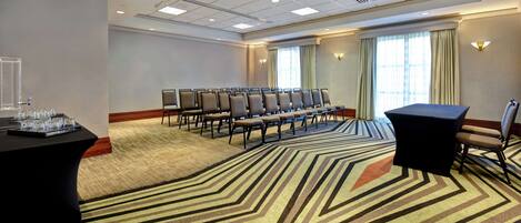 A conference room with a carpeted floor, rows of chairs, a table with a black tablecloth, and a window with curtains.