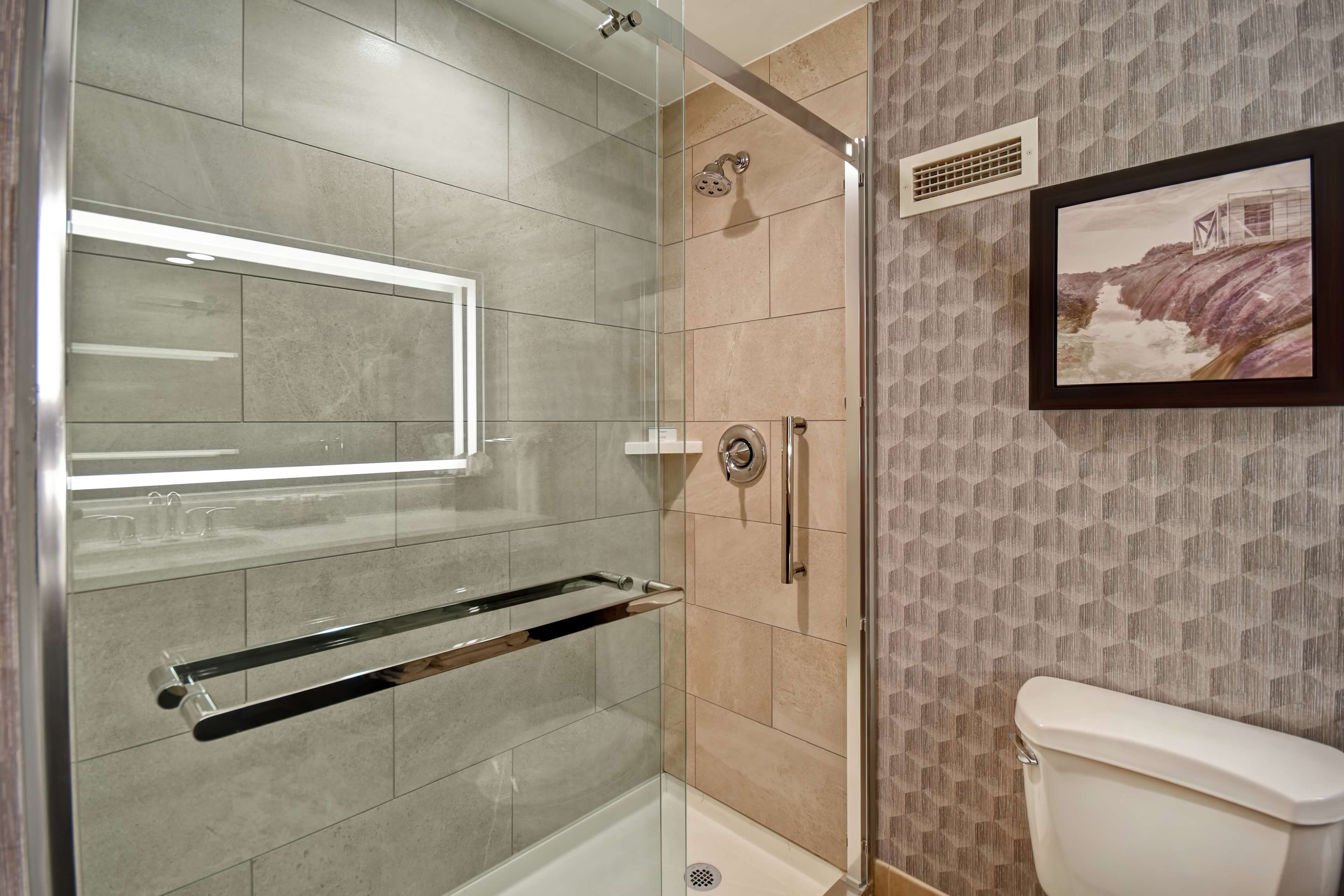 A modern bathroom with a glass shower enclosure, a toilet, and a framed picture on the wall.