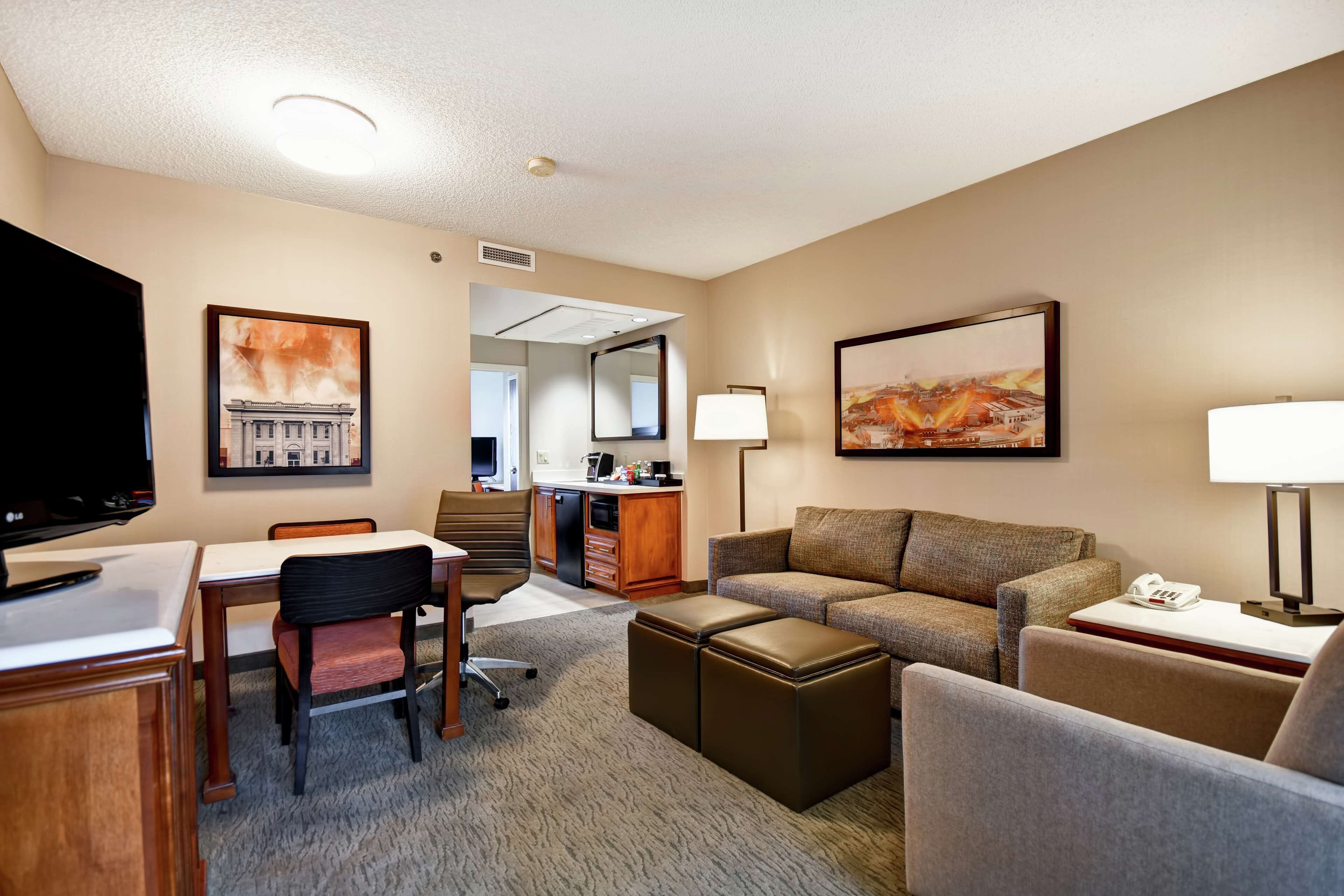 A hotel room with a dining area, a sofa set, a TV, a desk, and a bathroom visible through an open door.