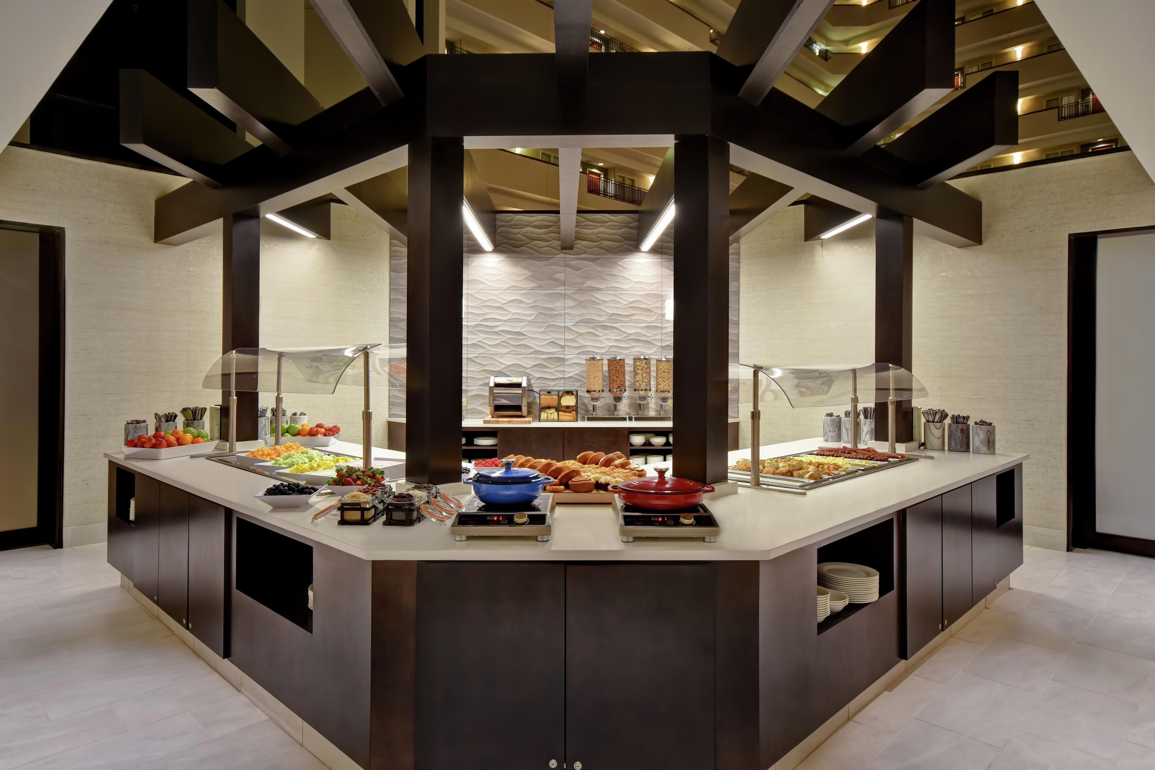 Um buffet de café da manhã moderno com diversas opções de comida, uma área central de serviço e design de interiores contemporâneo.