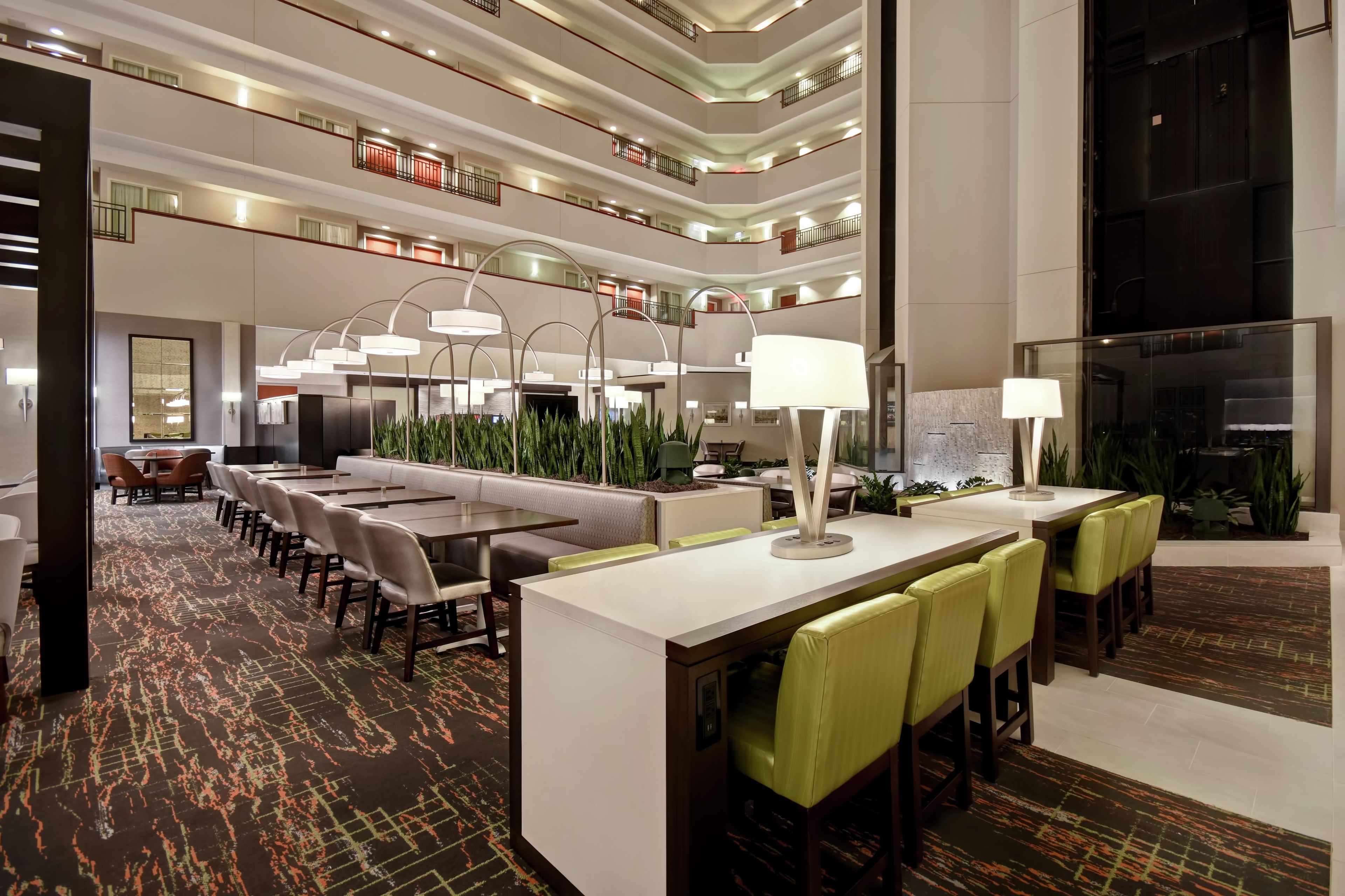 Un vestíbulo de hotel con un mostrador de recepción alargado, varias zonas de estar y un techo alto con luminarias.