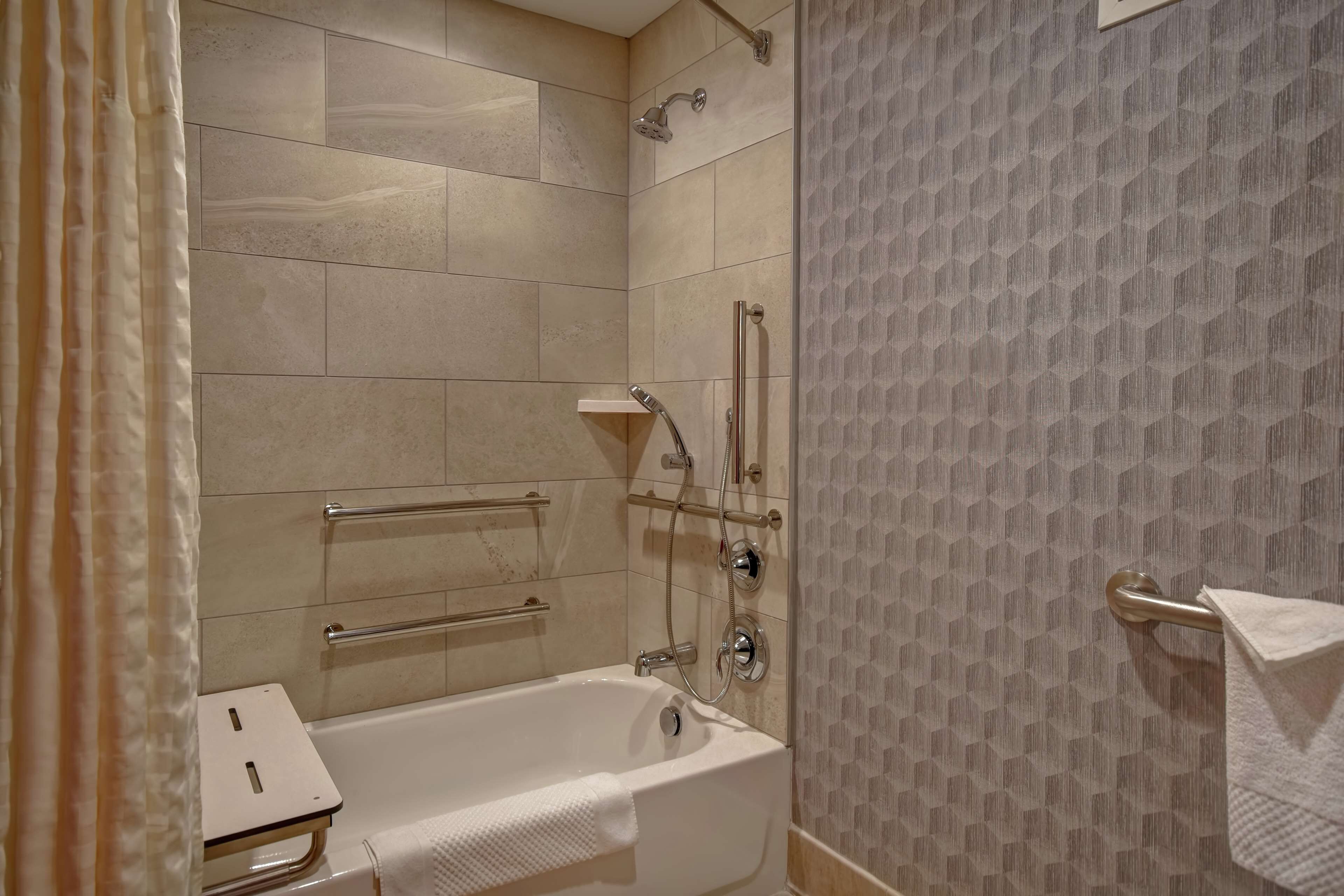 A modern bathroom with a bathtub, shower, and handrails.