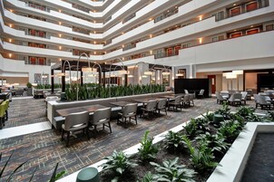 Un hall de hotel de varios niveles con zonas de estar, una recepción y una pantalla de televisión.