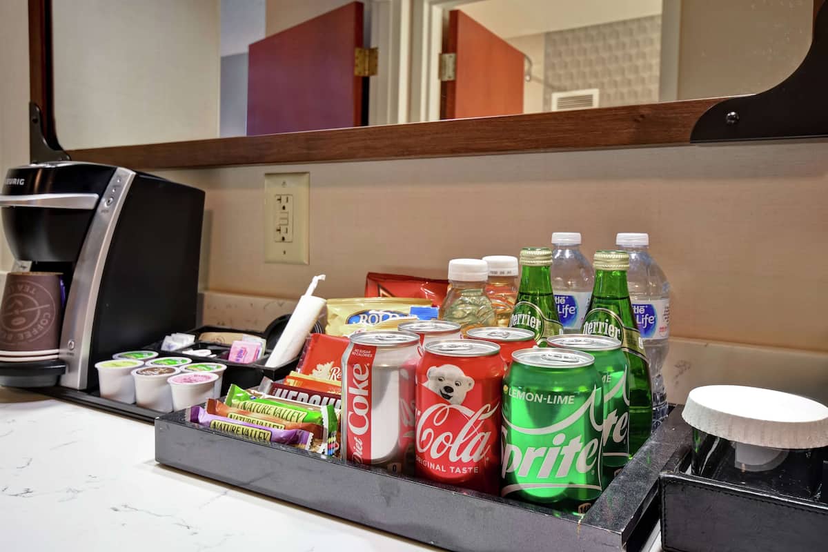 A minibar with various beverages and snacks, including cans of Coca-Cola, Sprite, Perrier, and bottled water.