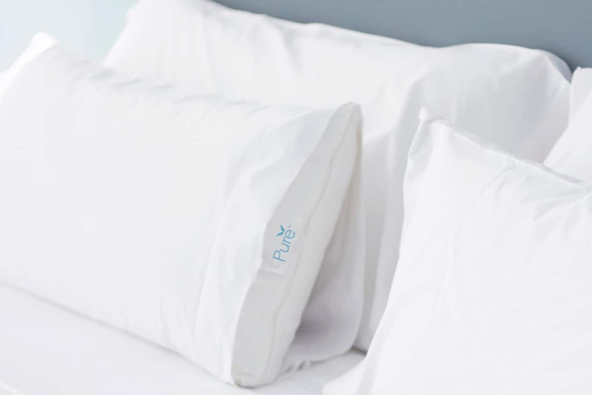 A white bed with pillows, one of which has a label that reads "Pure."