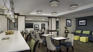 Un comedor moderno con una barra larga, varias mesas y sillas. Hay cuadros en las paredes y un sofá con cojines.