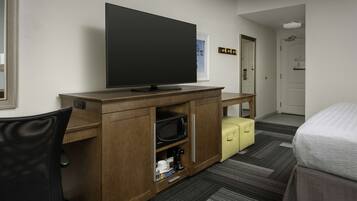 Hotelkamer met een televisie op een houten standaard, een magnetron, een koffiezetapparaat, een gele koffer en een bed.